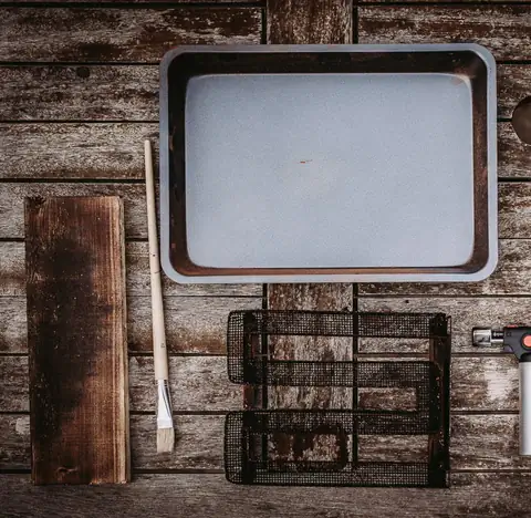 Mesa de madera con una bandeja de horno, un generador de humo frío de rejilla, una tabla y un pincel