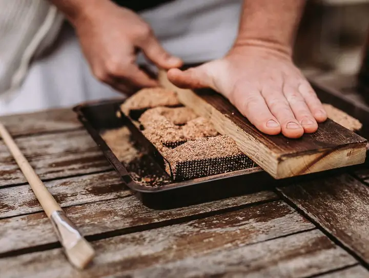 Una mano presiona con una tabla de madera el serrín dentro del generador